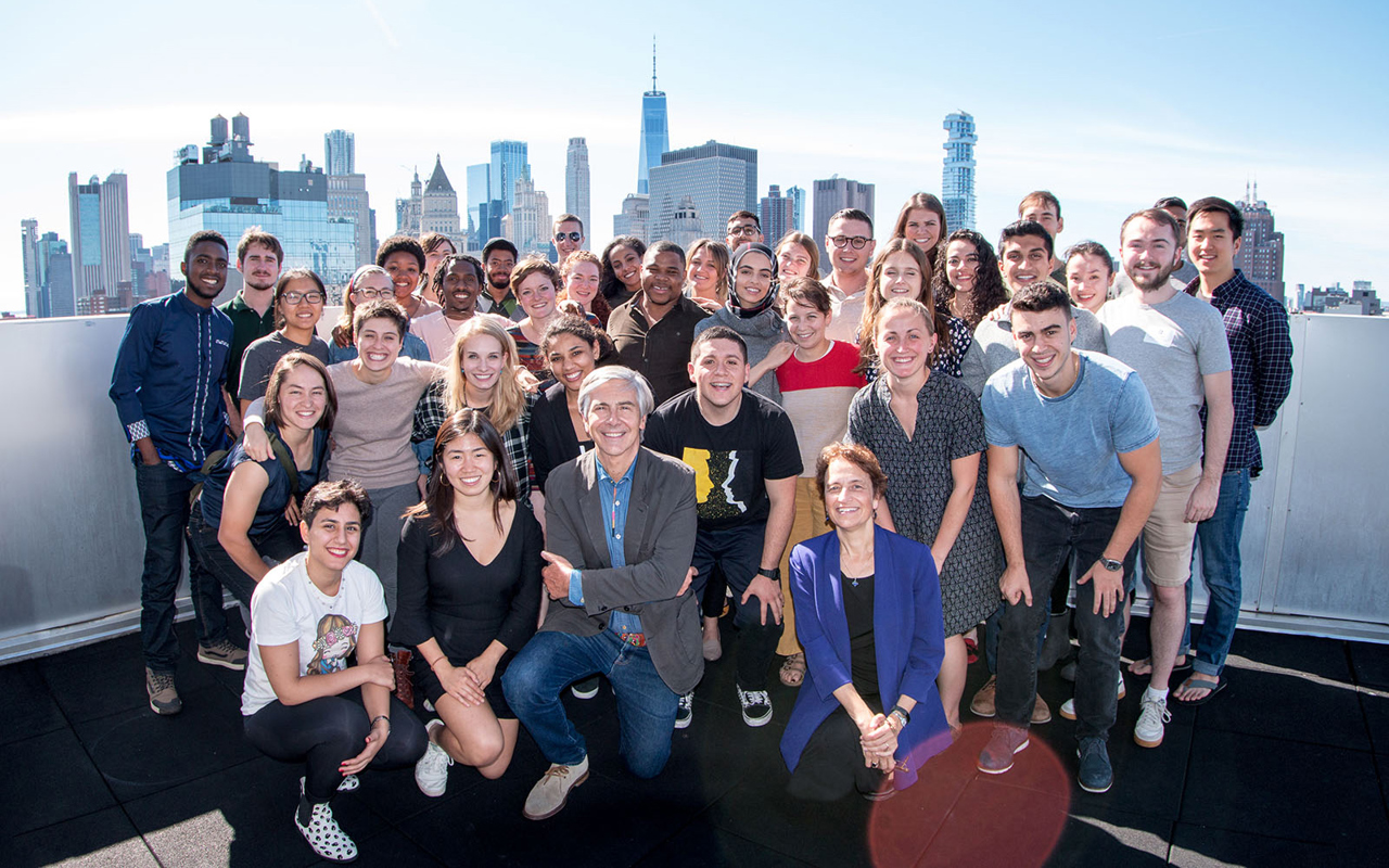 Large group of a group smiling and posing in front of NYC skyline.