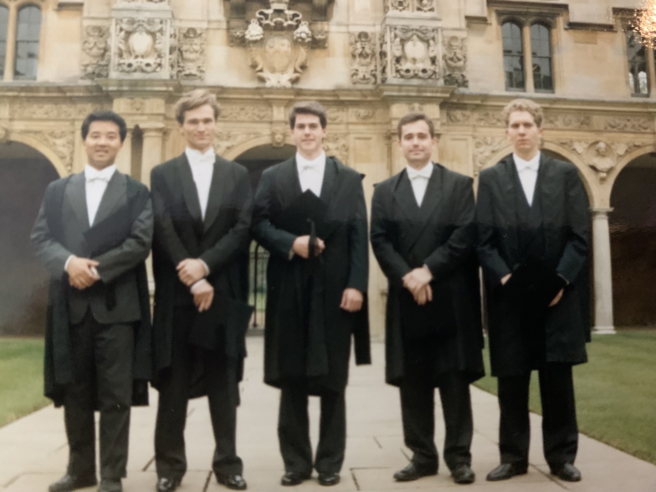 A group of 5 students stood in graduation attire before a building in Oxford.