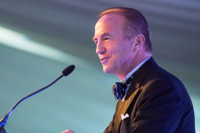 An image of John McCall MacBain, one of the Rhodes Trust's Second Century Founders. He is in a suit and bowtie speaking at a podium at an event.