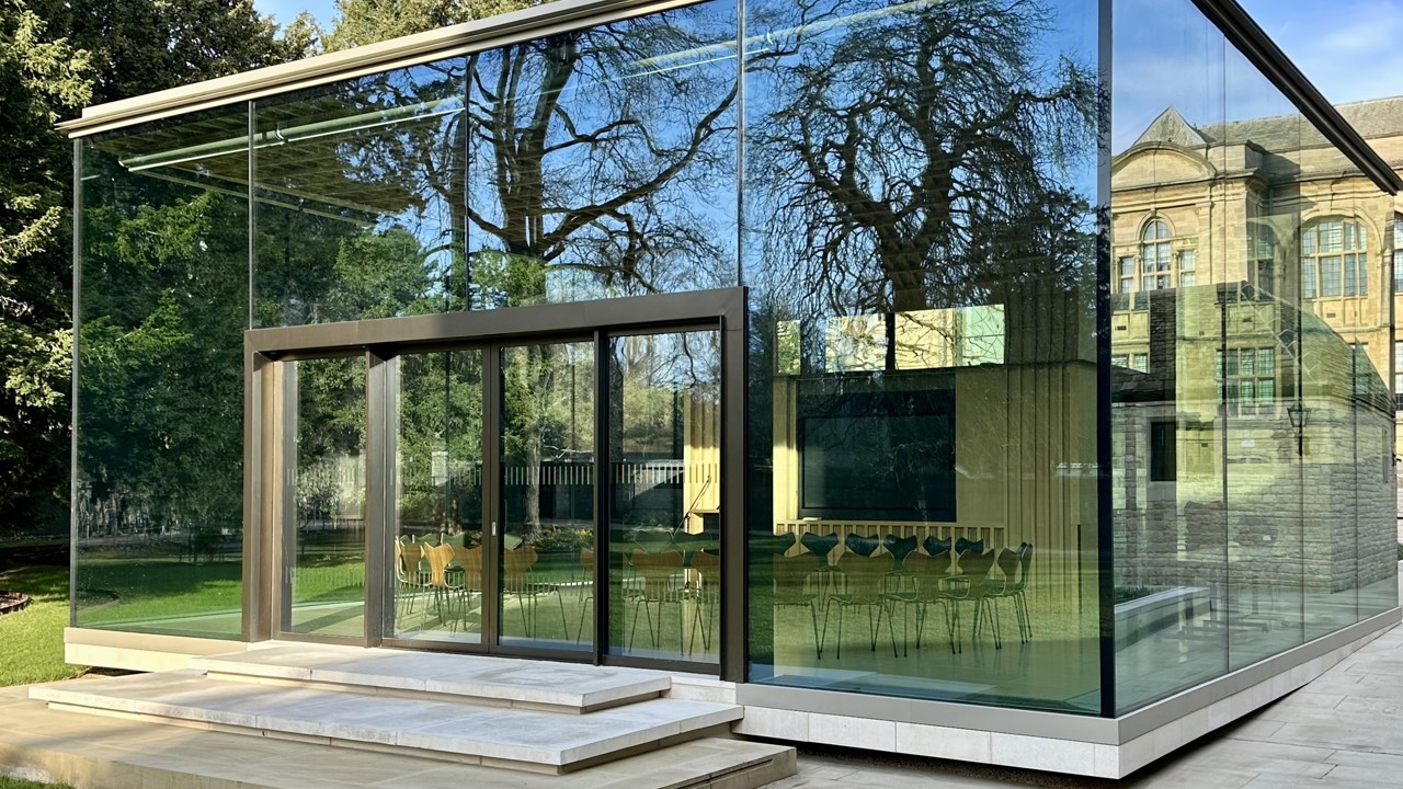 View of the Glass Pavilion from the West Lawn with a circle of chairs inside the room.