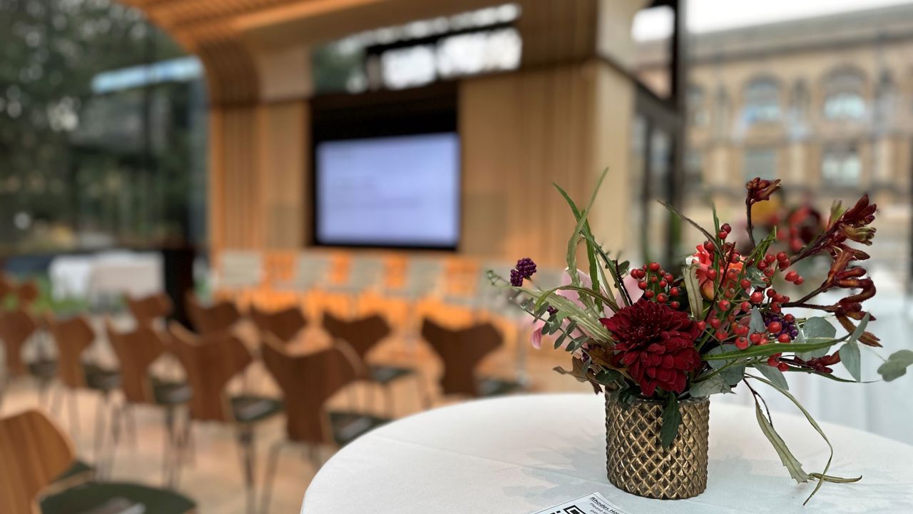 Glass Pavilion with poseur table and flowers in the foreground and theatre style seating and screen in the background.